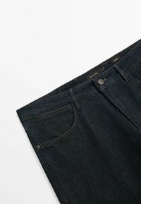 Mörka denimjeans har en klassisk design med fem fickor, synlig sömnad och en metallknappslåsning. Tyget har en mjuk textur.