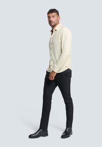 Lichtbeige overhemd met knopen en een subtiele textuur, gecombineerd met strakke zwarte broeken en elegante zwarte laarzen.