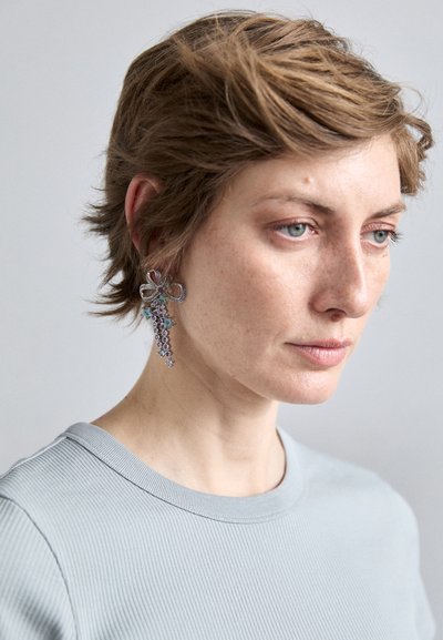 Textured light blue shirt worn with a large silver earring featuring a floral design and cascading multicolored gemstones.