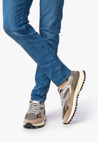 Zapatillas grises y topo con paneles de malla y ante, suela texturizada y acentos contrastantes. Llevadas con unos jeans ajustados azules.