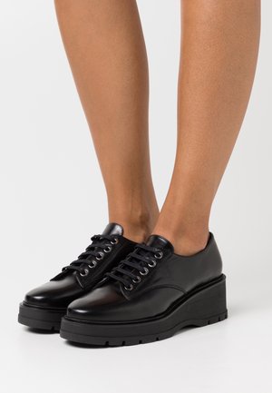 Zapatos de plataforma de cuero negro con punta redonda, cordones redondeados, parte superior texturizada y suela de goma negra gruesa.