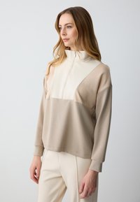 Beige en crèmekleurige half-zip pullover met lange mouwen en een relaxte pasvorm, met een diagonaal kleurblokontwerp en een gladde textuur.