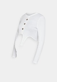 Vit kortärmad skjorta i mjukt tyg, med en rundad utskärning vid midjan och tre bruna knappar längs halslinningen.