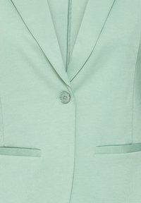 Blazer vert menthe avec une fermeture à un bouton et deux poches fendues horizontales à l'avant, doté d'un col cranté classique.