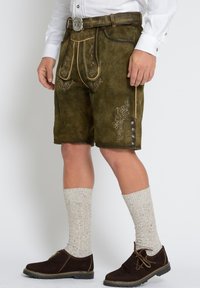 Bruine leren shorts met geborduurde ontwerpen, zijzakken en knopen aan de zijkant. Gecombineerd met gebreide lichtgekleurde sokken en donkere schoenen.