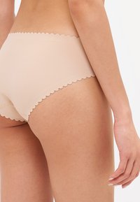 Culotte beige a vita alta con bordi scallopati. Il tessuto sembra liscio ed elastico, offrendo un aspetto aderente con minime cuciture visibili.