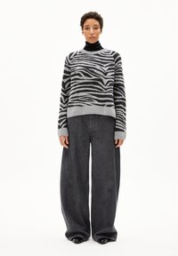 Schwarzer und grauer, gestreifter Pullover mit Rundhalsausschnitt, kombiniert mit grauen Jeanshosen im weiten Schnitt und schwarzen, spitzen Schuhen.
