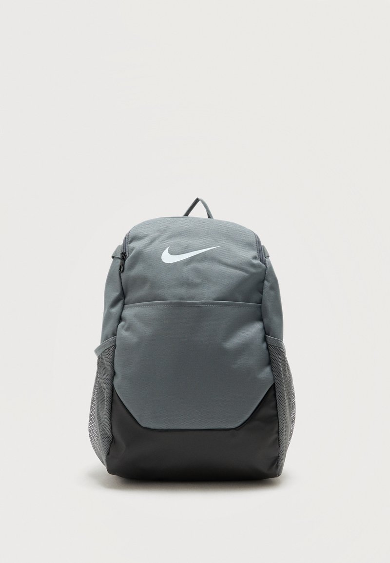 Γκρι και μαύρο σακίδιο Nike με μπροστινή τσέπη, δίχτυ πλαϊνές τσέπες, πάνω λαβή και λευκό λογότυπο Nike swoosh σε απλό φόντο.