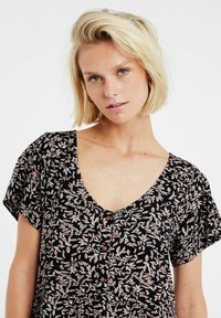 Schwarzes Kurzarmkleid mit V-Ausschnitt, versehen mit einem floralen Muster in Weiß und Pink sowie braunen Knopf-Akzenten auf der Vorderseite.