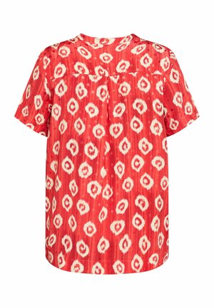 Sarkanais īsām piedurknēm blūze ar strukturētu rakstu, kas satur baltas un gaiši bēžas ovālas formas. Tam ir apaļš izgriezums un brīvs piegriezums.