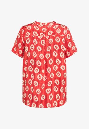 Sarkanais īsām piedurknēm blūze ar strukturētu rakstu, kas satur baltas un gaiši bēžas ovālas formas. Tam ir apaļš izgriezums un brīvs piegriezums.