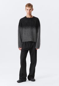 Pull gris ombré à manches longues, coupe décontractée, et texture duveteuse, associé à un pantalon noir à rayures et des chaussures au design texturé unique.