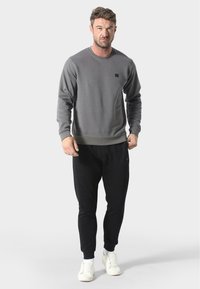 Harmaa collegemekko pyöreällä kaula-auolla, ribbaidoiduilla hihoilla ja helmalla, yhdistetty mustiin jogger-housuihin ja valkoisiin lenkkareihin. Vähäinen logoyksityiskohta rinnassa.
