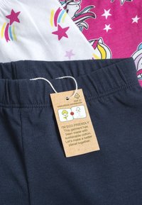 Pantalons en coton bleu marine avec une taille élastique et une étiquette indiquant qu'ils sont en coton écologique et durable. Superposés avec un tissu à motifs au-dessus.