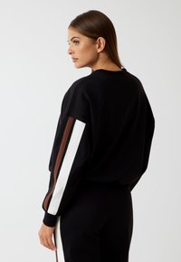 Felpa nera con vestibilità rilassata, caratterizzata da accenti a strisce marroni e bianche sulle maniche. Tessuto dalla texture liscia e design a collo rotondo.