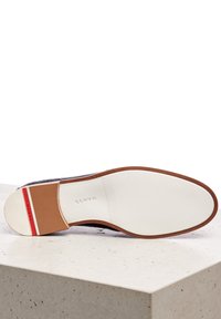 Brown leather shoe sole with a textured surface, featuring a white rubber bottom and a red accent stripe with embossed branding.