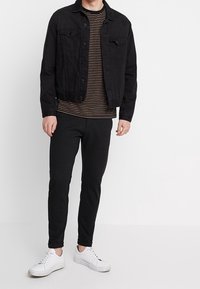 Schwarze Jeansjacke, gestreiftes schwarz-beiges T-Shirt, schwarze tapered Hose und weiße Sneakers. Minimalistisches Design, lässige Passform.