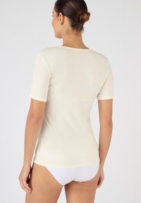 T-shirt a maniche corte color crema realizzata in morbido tessuto, con scollatura tonda e design aderente, caratterizzata da una texture liscia e uno stile minimalista.