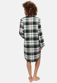 Camisa de cuadros verde y blanca de gran tamaño con mangas largas, con un dobladillo redondeado y aberturas laterales para facilitar el movimiento.