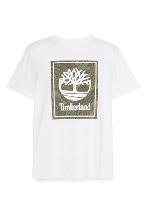 Witte katoenen T-shirt met een groot groen en wit Timberland-boomlogo binnen een rechthoekig kader, tegen een gestructureerde groene achtergrond.