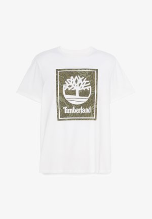 Weißes Baumwoll-T-Shirt mit großem grün-weißen Timberland-Baum-Logo innerhalb eines rechteckigen Rahmens, vor einem strukturierten grünen Hintergrund.