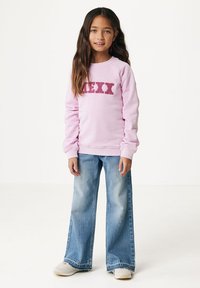 Helles rosa Sweatshirt mit "MEXX" in strukturierten roten Buchstaben, kombiniert mit weit geschnittenen, ausgewaschenen blauen Jeans und hellen Sneakers.