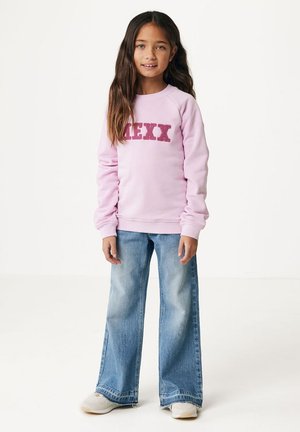Felpa rosa chiaro con "MEXX" in lettere rosse testurizzate, abbinata a jeans a gamba larga in blu sbiadito e sneakers di colore chiaro.