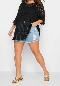 Svart öppenstickad topp med lös passform och en vågig nederkant. Matchad med ljusblå slitna denimshorts och guldiga sandaler.