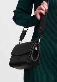 Černá kožená kabelka přes tělo s překlápěcí klopou, texturovaným tělem, nastavitelným popruhem a kovovými detaily se zavěšeným logem.