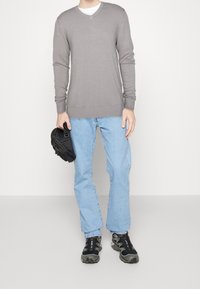 Gray long-sleeve V-neck sweater, light blue straight-leg jeans, and black sneakers. Holding a small black bag. Minimalist overall appearance.