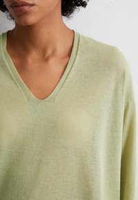 Maglione verde chiaro a collo a V con una texture morbida, caratterizzato da una vestibilità rilassata e un delicato motivo a maglia, che enfatizza calore e comfort.