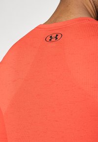 Κόκκινο αθλητικό μπλουζάκι με υφασμάτινη υφή, εφαρμοστή σχεδίαση και μαύρο λογότυπο στην πλάτη. Κοντά μανίκια και στρογγυλός λαιμός.