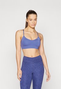 Sujetador deportivo azul con tirantes finos y escote redondeado, confeccionado en una tela suave; combinado con leggings azules estampados que tienen una cinturilla alta.