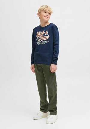 Chemise à manches longues marine avec un texte graphique blanc et orange, accompagnée d'un pantalon vert olive et de baskets blanches. Tenue simple et décontractée.