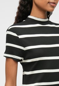 Fekete-fehér csíkozott bordázott felső, magas nyakkal és rövid ujjakkal, textúrált anyaggal és kontrasztos csíkokkal.