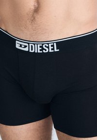 Black Diesel boxer briefs with a white logo on the elastic waistband, featuring a smooth, stretchy fabric and a tight fit.