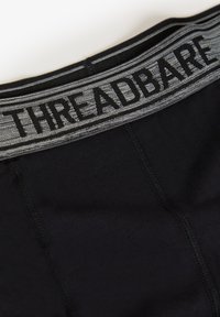 Schwarze Baumwoll-Boxershorts mit einem grauen elastischen Bund, der "THREADBARE" in fettgedruckten schwarzen Buchstaben zeigt. Glatte Textur und minimalistisches Design.