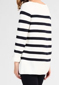 Bluza w paski wykonana z teksturowanej tkaniny, z szerokimi granatowo-białymi poziomymi paskami, dekoltem w łódkę i podwiniętymi rękawami.