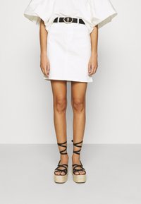 Mini falda de mezclilla blanca combinada con sandalias de plataforma negras con tiras entrecruzadas y detalles de esparto. Cinturón negro con hebilla circular.