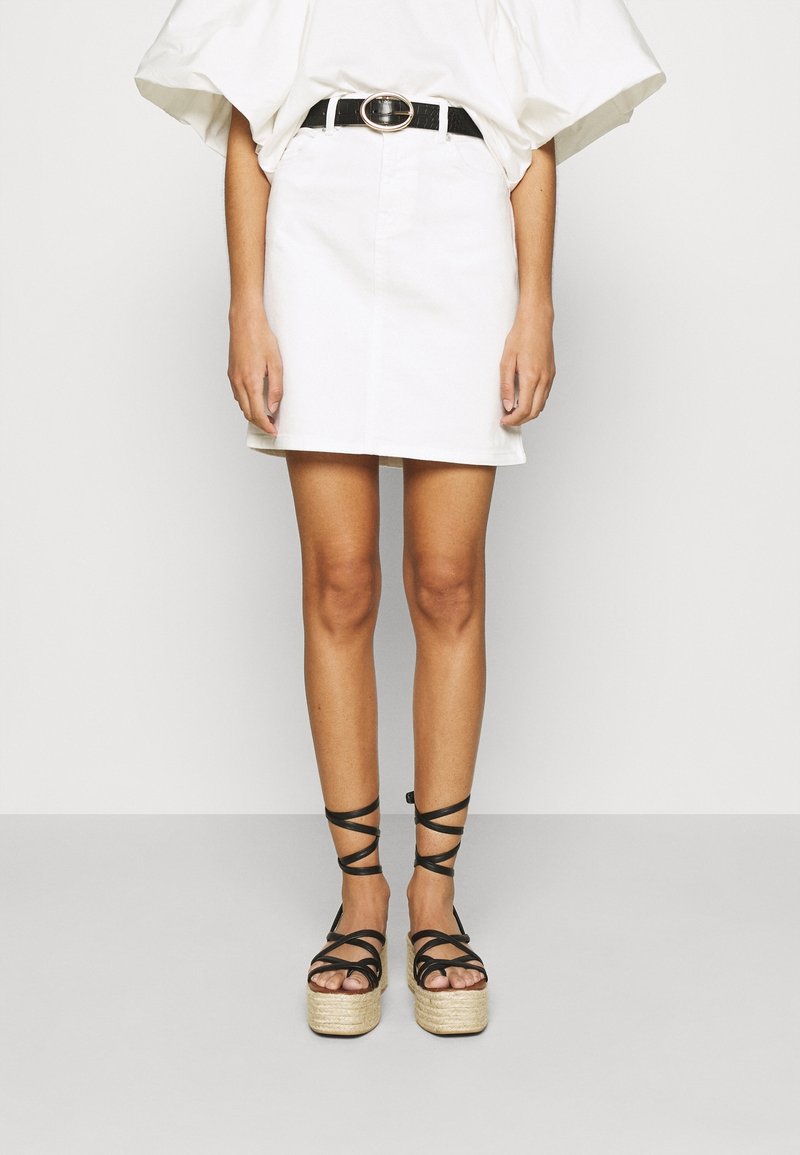 Mini falda de mezclilla blanca combinada con sandalias de plataforma negras con tiras entrecruzadas y detalles de esparto. Cinturón negro con hebilla circular.