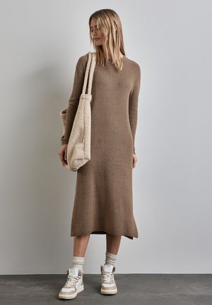 Langes, braunes, geripptes Sweatkleid mit lockerer Passform, kombiniert mit weißen und beigen Sneakern sowie einer beigen, strukturierten Schultertasche.