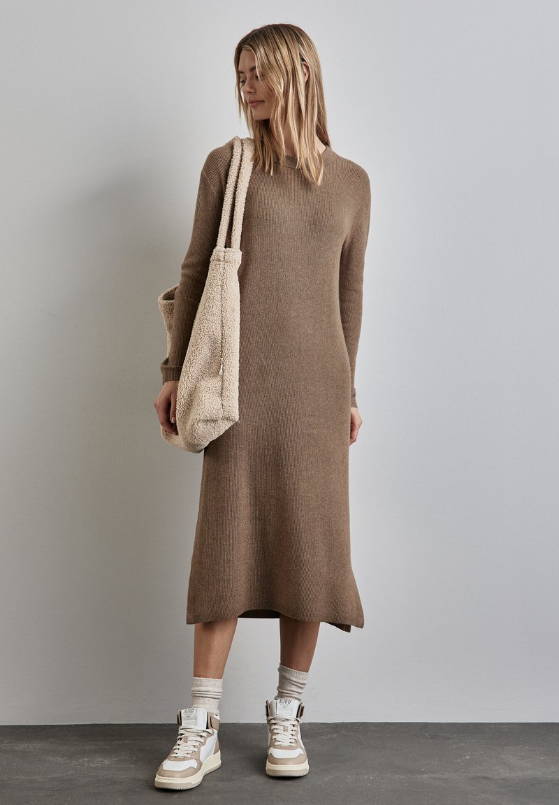 Langes, braunes, geripptes Sweatkleid mit lockerer Passform, kombiniert mit weißen und beigen Sneakern sowie einer beigen, strukturierten Schultertasche.