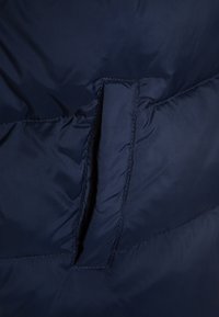 Mörkblå quiltad tyg med en vertikal slitsficka som detaljeras av sömmar på den vadderade ytan.