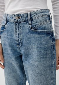 Světle modré džíny z denimu s vysokým pasem, vybavené zapínáním na knoflík, dvěma předními kapsami a jemnými detaily vymývání na látce.