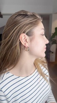 Sølvringformet ørepynt med et geometrisk mønster og en polert finish. Håret er bølgete, og bakgrunnen er mykt uskarp.