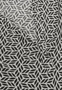 Schwarz-weißer Stoff mit einem Blattmuster, im V-Ausschnitt-Design und kontrastierenden Stickdetails. Weiches, strukturiertes Material.
