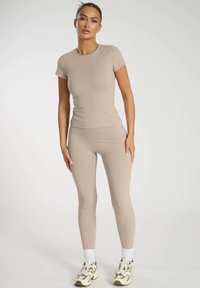 Beige aktivklädesset bestående av en figursydd kortärmad topp och högmidjade leggings, tillverkade av slätt, elastiskt tyg.