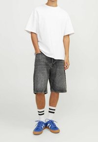 Henkilö seisoo päällään valkoinen oversize t-paita, mustat farkkuhousut, valkoiset sukat mustilla raidoilla ja siniset lenkkarit valkoisilla raidoilla.