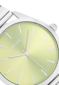 Montre-bracelet en acier inoxydable argenté avec un cadran dégradé vert clair, des index horaires argentés et des aiguilles fines, présentant une finition polie et une couronne.