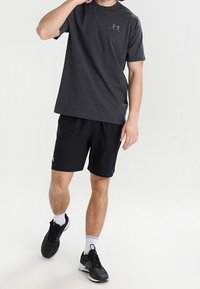 Mörkgrå kortärmad T-shirt med en liten logga, ihopparad med svarta sportshorts och svarta sneakers med vita detaljer.